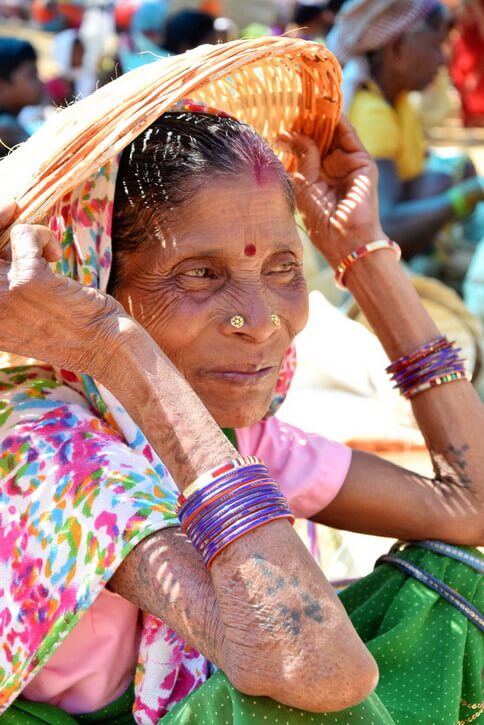 Une femme de la tribu Dhurwa avec des tatouges aux bras et s'abritant sous un panier