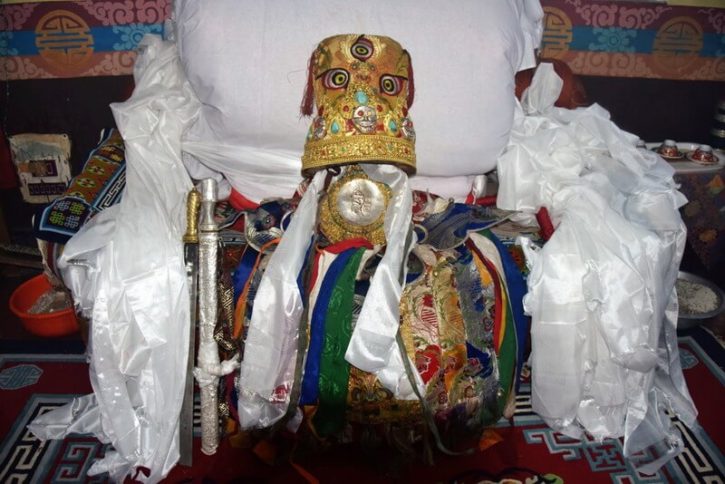 La coiffe dorée et les habits de l'oracle Bouddhiste sur un fauteuil décoré