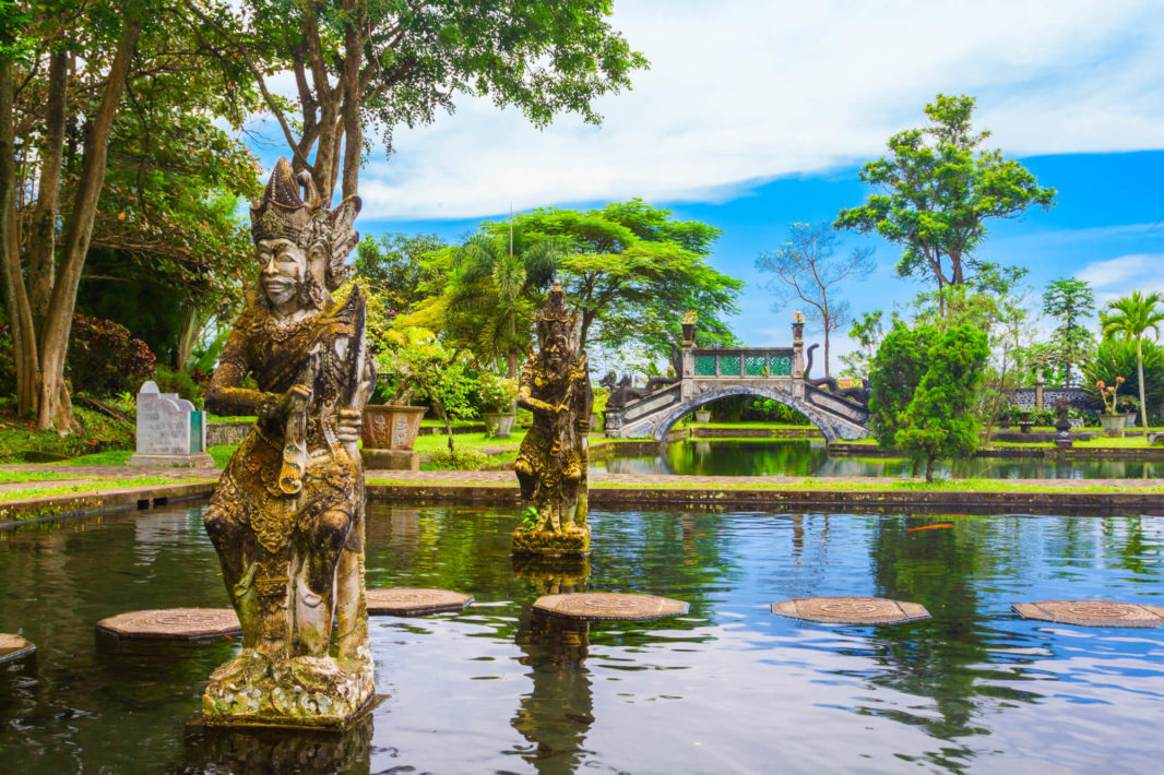 Balinese stone statues on the water, old stone bridge and tropical trees